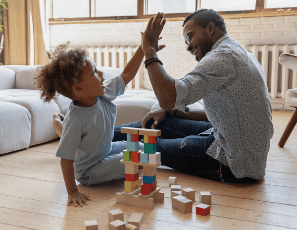 A man and a child sitting on the floor playing with wooden blocks
