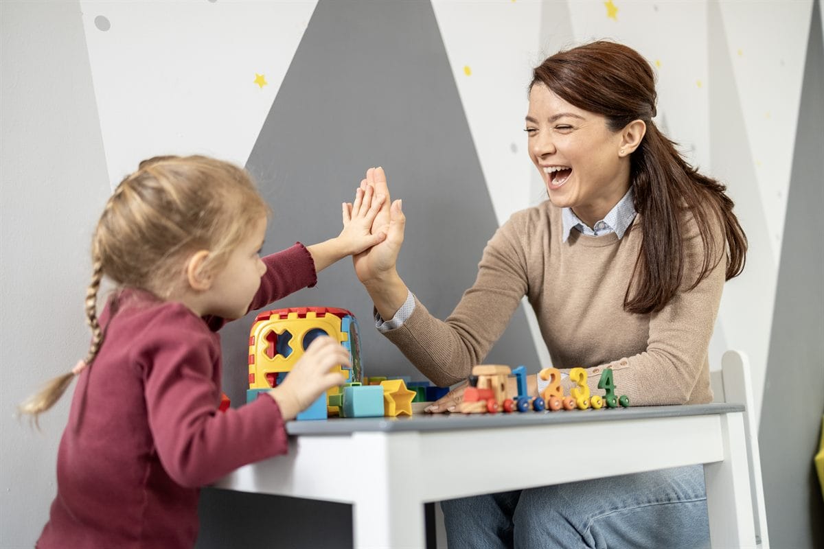 A preschool teacher and child high-fiving and enjoying playtime